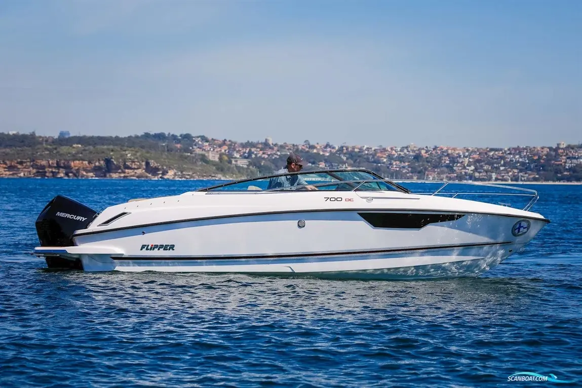 A white Flipper 700 DC boat with a Mercury engine, cruising on clear water, with a coastal city visible in the background.
